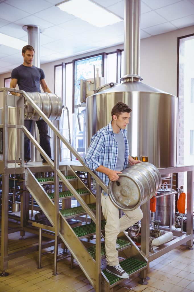 Young men carrying keg smiling at camera in the factory