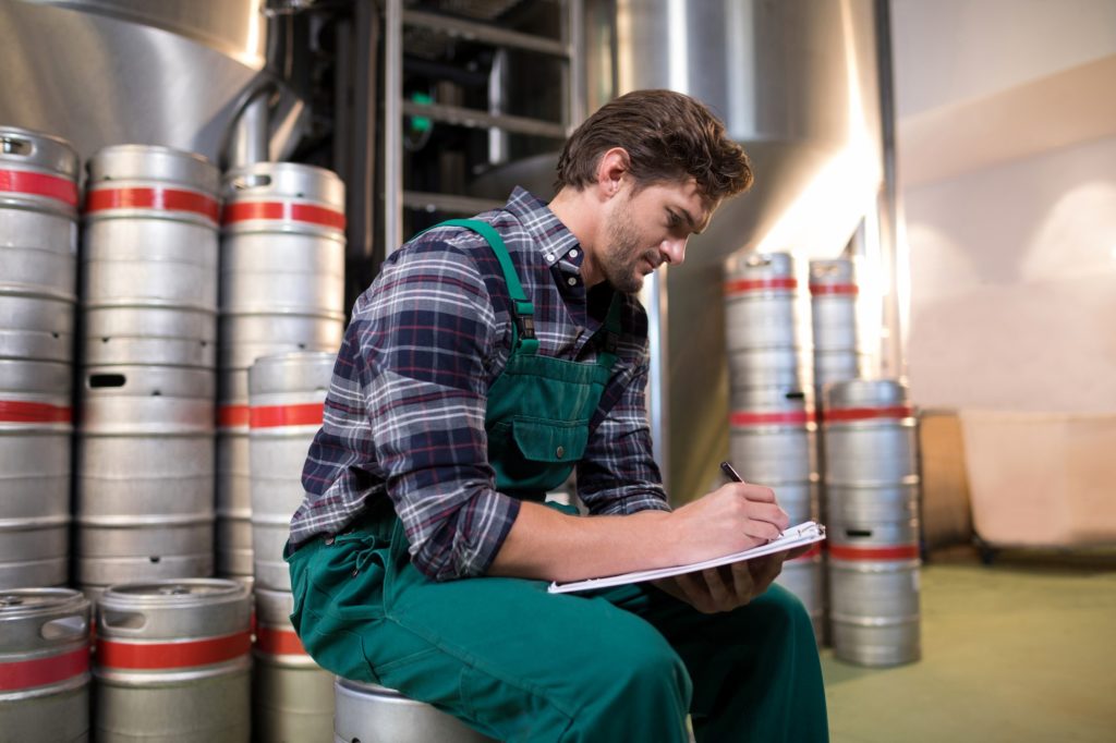 Worker writing on paper while sitting on keg at warehouse